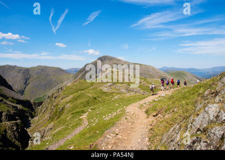 Hikers hiking on Corridor Route mountain path over Sty Head pass below Great End in mountains of Lake District National Park. Cumbria England UK Stock Photo
