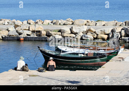 Elderly man and woman sitting on the pier. boats in the background. Porto Cervo, Sardinia, Italy Stock Photo