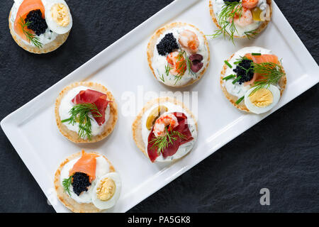 Selection of cocktail blinis with salmon, cured bresaola, crayfish, caviar, quail eggs and sour cream - gourmet party food - top view Stock Photo