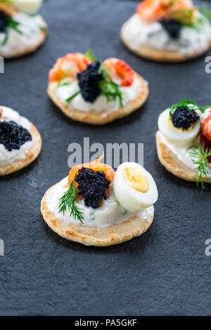 Selection of cocktail blinis with salmon, cured bresaola, crayfish, caviar, quail eggs and sour cream - gourmet party food Stock Photo