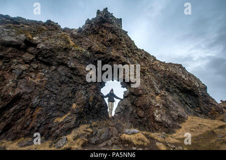 Young man stands in rock arch, volcanic rock on the beach of Djúpalónssandur, Snæfellsnes peninsula, West Iceland, Iceland