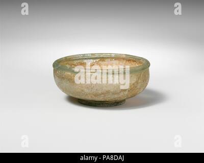 Glass bowl. Culture: Roman. Dimensions: Overall: 1 1/4 x 2 7/8 x 1 3/8 in. (3.2 x 7.3 x 3.5 cm). Date: ca. 3rd century A.D..  Colorless with pale greenish tinge.  Thick, rounded rim, with inner lip; short, convex, curving sides to body; solid pad base; flat bottom, with small kick at center and pontil mark.  Intact; many pinprick bubbles; pitting, dulling, and iridescent weathering on exterior, slight soil encrustation and creamy brown weathering on interior. Museum: Metropolitan Museum of Art, New York, USA. Stock Photo