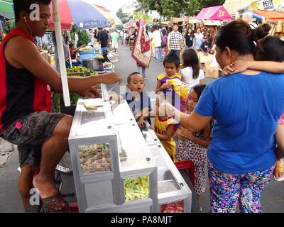 QUEZON CITY, PHILIPPINES - NOVEMBER 22, 2015: Children buy candies and sweets from a street vendor Stock Photo