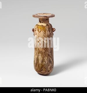 Glass alabastron (perfume bottle). Culture: Greek, Eastern Mediterranean or Italian. Dimensions: H.: 5 1/8 in. (13 cm). Date: mid-4th-early 3rd century B.C..  Translucent pale honey brown, with handles in darker honey brown; trails in opaque yellow, opaque turquoise blue, and opaque white.  Broad horizontal rim-disk, with radiating tooling marks on underside; cylindrical neck, expanding downwards; narrow sloping shoulder; straight-sided cylindrical body, with slight upward taper; convex bottom; below shoulder, two vertical ring handles, not pierced through, with short pointed trails, applied o Stock Photo