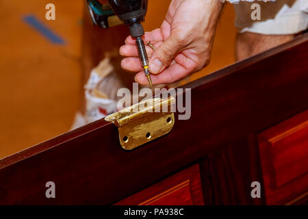 Screwdriver installs screw on stainless door hinges with wooden swing door for interior design. Stock Photo