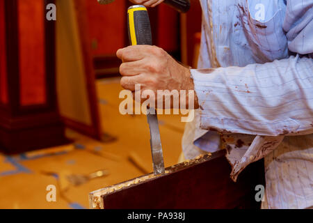 Man carpenter makes a hole in the wooden a door for a hammer and chisel. Close-up Stock Photo