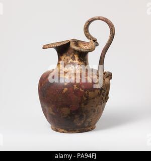Bronze oinochoe (jug). Culture: Greek. Dimensions: H.: 8 15/16 in. (22.7 cm). Date: ca. 460 B.C..  The handle attachment is in the form of a frontal siren.  The function of a handle attachment is to secure the base of the handle securely to the body of the vase; a broad surface provides a stronger bond. From a purely mechanical viewpoint, the siren with its extended wings fulfills the purpose effectively. She wears a silver fillet. Museum: Metropolitan Museum of Art, New York, USA. Stock Photo
