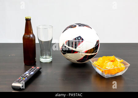 People prepared to watch football on TV with beer. There's beer on the table, ball, TV remote, snacks. Craft beer. Light background. Stock Photo