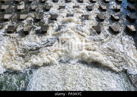 Powerful flow of foaming water is crashing on concrete stones-breakwaters near the dam. Stock Photo