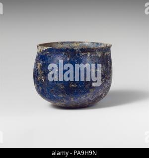Glass cup. Culture: Roman. Dimensions: 2 1/2 in. (6.4 cm)  Diameter: 3 1/4 × 3 1/16 in. (8.3 × 7.8 cm). Date: 1st century A.D..  Translucent blue.  Knocked off, horizontal rim, with slight bulge below; uneven, convex side to body; rounded bottom, with small concave center.  Faint wheel-abraded horizontal lines, one 0.4 cm below rim, two more on body at point of greatest diameter.  Broken and repaired; few bubbles; dulling and whitish, iridescent weathering covering much of surfaces.  Stands aslant on bottom. Museum: Metropolitan Museum of Art, New York, USA. Stock Photo