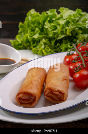 Spring rolls accompanied by lettuce, soy sauce and cherry tomatoes on wooden background Stock Photo