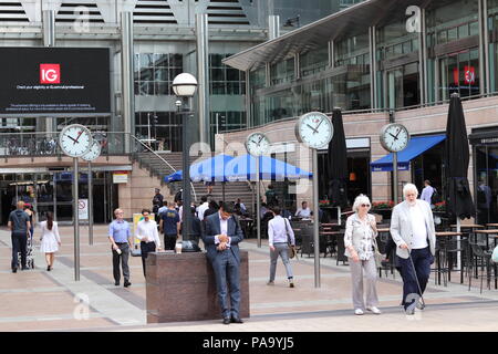 People walking past clocks in Canary Wharf, Londn Stock Photo