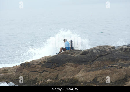 Two young boys sitting on the rocks near breaking surf in Ocean Point, Boothbay, Maine, USA Stock Photo