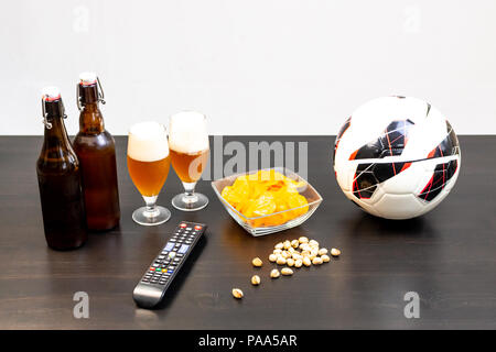 People prepared to watch football on TV with beer. There's beer on the table, ball, TV remote, snacks. Craft beer. Light background. Stock Photo