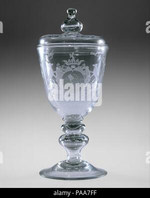 Covered goblet. Culture: American. Dimensions: H. 11 1/4 in. (28.6 cm). Maker: New Bremen Glass Manufactory (1784-1795); John Frederick Amelung (active 1784-ca. 1791). Date: 1788.  German glassmaker John Frederick Amelung (1741/2-1798) opened a glasshouse in western Maryland in 1787, responding to America's desire for economic independence from Britain and the need to develop domestic manufactures. Within a few years, he was producing a variety of window glass, bottles, and tableware at his New Bremen factory. Some of Amelung's products feature elaborate engraved decoration in the Germanic sty Stock Photo