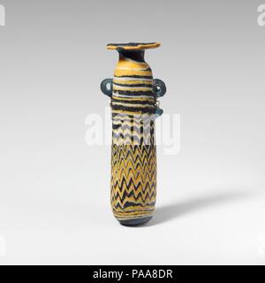 Glass alabastron (perfume bottle). Culture: Greek, Eastern Mediterranean. Dimensions: H.: 4 3/16 in. (10.6 cm). Date: 5th century B.C..  Translucent light blue, with handles in same color; trails in opaque yellow and opaque white.  Broad horizontal rim-disk, with radiating tooling marks on upper surface; short cylindrical neck; rounded shoulder; straight-sided cylindrical body with upward taper; convex bottom; two vertical ring handles with knobbed tails, applied over trail decoration.  Yellow trail attached at edge of rim-disk; a white trail overlaid with yellow wound unevenly around neck and Stock Photo