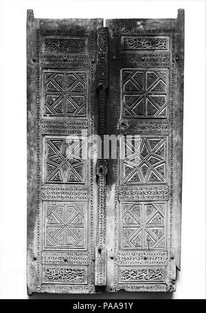 Pair of Carved Doors. Dimensions: H. 59 1/4 in. (150.5 cm)  W. 32 in. (81.3 cm)  Gr. D. 3 1/2 in. (8.9 cm)  Wt. 48 lbs (21.8 kg). Date: dated 1466.  These teak doors consist of several decorative and epigraphic panels joined together and inset into a frame. The pair of square panels with geometric designs reflect carved Iranian woodwork of the fifteenth century. A cenotaph, dated 1473, now in the Museum of Art, Rhode Island School of Design, displays very similar designs and inscriptions. The scrolling vines framing the panels and on the vertical bar share qualities with wave motifs seen in Ti Stock Photo