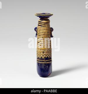 Glass alabastron (perfume bottle). Culture: Greek, Eastern Mediterranean. Dimensions: H.: 4 1/4 in. (10.8 cm). Date: late 6th-5th century B.C..  Translucent cobalt blue, with handles in same color; trails in opaque yellow and opaque turquoise blue.  Broad, inward sloping rim-disk, with radiating tool marks on upper surface and uneven edge around mouth; short cylindrical neck with downward taper; narrow rounded shoulder; straight-sided cylindrical body, tapering upwards; convex bottom; two vertical ring handles with knobbed tails, applied over trail decoration.  Turquoise blue trail attached at Stock Photo