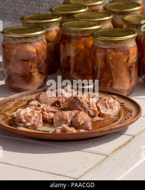 Canned meat in a glass jar on a white wooden table. Next plate with meat Stock Photo
