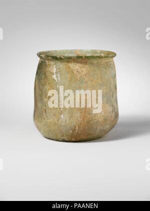 Glass cup. Culture: Roman. Dimensions: H.: 3 1/16 in. (7.8 cm). Date: 2nd-3rd century A.D..  Translucent pale blue green.  Thickened, everted rim, with rounded lip; undulating side to body, expanding downwards, then curving in to flat bottom with small kick at center.  Intact; a few bubbles; some brilliant iridescence on exterior but most of surfaces covered with limy encrustation and weathering. Museum: Metropolitan Museum of Art, New York, USA. Stock Photo