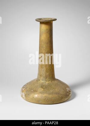 Glass perfume bottle. Culture: Roman. Dimensions: H.: 6 3/4 in. (17.1 cm). Date: 2nd-3rd century A.D..  Uncertain (colorless with yellow green tinge?).  Rim folded out, down, round, and pressed into mouth; tall cylindrical neck, expanding downwards; broad, bell-shaped body; concave bottom.  Intact; some bubbles; dulling, surfaces covered with weathering and iridescence. Museum: Metropolitan Museum of Art, New York, USA. Stock Photo