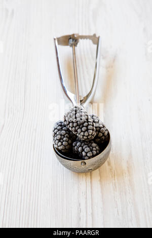 Icecream scoop with frozen blackberries on a white wooden background, side view. Close-up. Stock Photo