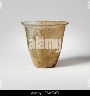 Glass cup. Culture: Roman. Dimensions: 3 7/16 in. (8.7 cm)  Diameter: 3 9/16 in. (9 cm). Date: 1st-2nd century A.D..  Colorless with faint greenish tinge.  Knocked-off rim; slightly bulging collar below rim; carinated sides tapering downward; concave bottom.  One fine horizontal wheel-cut line below collar 5/16 in. (8 mm) below rim), two more 1/16 in. (1 mm) apart further down body, 13/16 in. (21 mm) below rim, and another single line below just above turn 1 13/16 in. (46 mm) below rim.  Intact, except for one deep chip in rim; pinprick bubbles; almost unweathered on one side; elsewhere pittin Stock Photo
