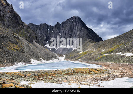 Frozen lake in mountain circus in front of peak. East Sayan. Russia Stock Photo