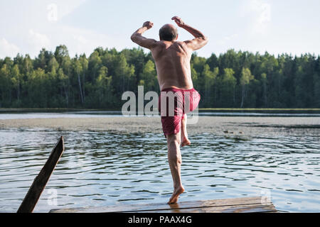 Mature man in red swimming clothes jumping into lake. having a good rest outdoor in vullage Stock Photo