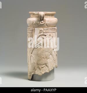 Levantine vessel with rampant goats and olive trees. Dimensions: H. 6 1/2 in. (16.4cm). Date: ca. late 2nd-early 1st millennium B.C..  Carved from a single piece of elephant ivory, this vessel takes the form of a tapering cylinder with a small handled cup on top. The cup has been damaged and may have had a second handle opposite the one which is preserved. The base of the vessel is likewise now missing. Carved in relief around the base of the vessel is a scene framed by decorative borders at top and bottom, showing two male goats grazing from trees. A third tree of the same type is represented Stock Photo