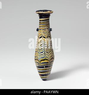 Glass alabastron (perfume bottle). Culture: Greek, Eastern Mediterranean. Dimensions: H.: 5 1/16 in. (12.9 cm)  Diam.: 1 7/16 x 1 1/4 in. (3.6 x 3.1 cm). Date: 2nd-1st century B.C..  Translucent blue, with handles in same color; trails in opaque yellow and opaque white.  Broad rim-disk, uneven and sloping inward with radiating tooling marks on upper and lower surfaces, and jagged, projecting inner lip to neck; cylindrical neck; straight-sided fusiform body expanding downward, then tapering in to pointed bottom; two elongated horizontal lug handles applied at top of body over trails; marvered b Stock Photo