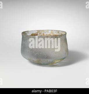 Glass cup. Culture: Roman. Dimensions: H.: 1 5/8 in. (4.1 cm)  Diam.: 2 1/4 in. (5.7 cm). Date: 1st-2nd century A.D..  Translucent pale blue.  Short, slightly everted, knocked-off rim; straight side expanding downwards, then curving sharply inwards; small, concave bottom.  On upper part of body, bands of horizontal wheel-abraded lines, extending from rim to undercurve.  Intact; pinprick bubbles; dulling, deep pitting, and some iridescent weathering on exterior, large patch of soiled encrusted weathering and iridescence on interior. Museum: Metropolitan Museum of Art, New York, USA. Stock Photo