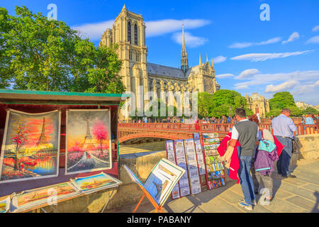 Paris, France - July 1, 2017: people looking at traditional Bouquiniste on the edge of Seine in front Notre-Dame cathedral. The Bouquinistes sell paintings of the Eiffel Tower and tourist souvenirs. Stock Photo