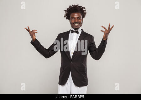 African well dressed singer or actor with afro hair style in classic style tuxedo and bow tie toothy smiling. Indoor, isolated studio shot on gray bac Stock Photo