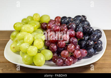 Black, red, green seedless grapes in a deep white bowl on a white tale waiting to be eaten for breakfast Stock Photo