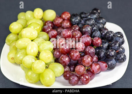 Black, red, green seedless grapes in a deep white bowl on a white tale waiting to be eaten for breakfast Stock Photo