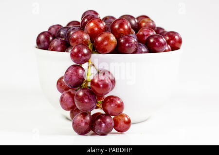 Red seedless grapes in a deep white bowl on a white tale waiting to be eaten Stock Photo