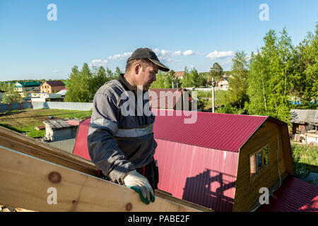 The builder stands on the roof of a wooden house and thinks how to put transverse lags Stock Photo