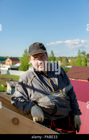 The builder stands on the roof of a wooden house and thinks how to put transverse lags Stock Photo