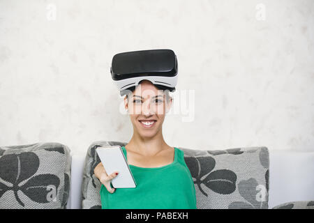 Beautiful disabled young woman with virtual reality goggles sitting on couch and preparing for playing video game. Stock Photo