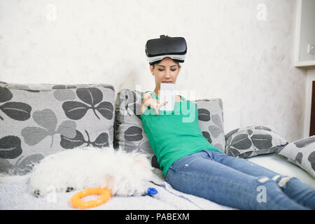 Beautiful disabled young woman with virtual reality goggles sitting on couch and preparing for playing video game. Stock Photo