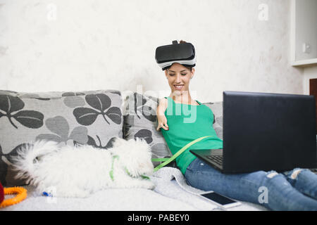 Beautiful disabled young woman with virtual reality goggles sitting on couch and preparing for playing video game. Stock Photo