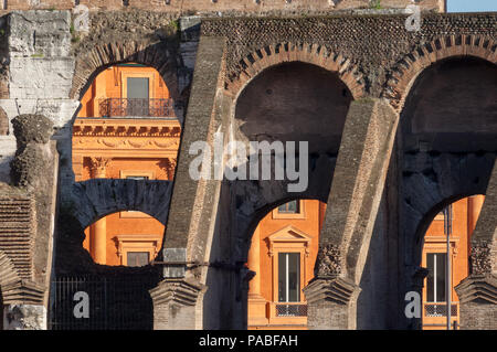 Arches of the eastern wall of the Colosseum frame a brightly coloured building on the Piazza dei Colosseo in Rome Stock Photo