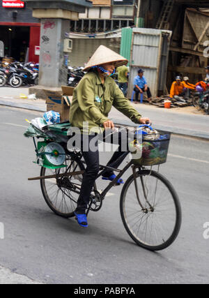 A Vietnamese woman wearing a straw conical hat riding her bicycle on a street in Ho Chi Minh City, Vietnam.