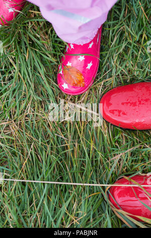 A girl in red rubber boots and a yellow raincoat runs through puddles ...