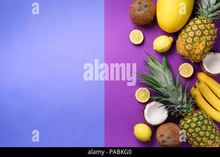 Exotic pineapples, coconuts, banana, melon, lemon, tropical palm and green monstera leaves on purple, violet background with copyspace. Creative layou Stock Photo