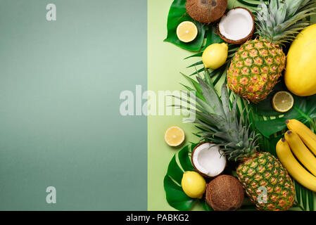 Exotic pineapples, coconuts, banana, melon, lemon, tropical palm and monstera leaves on green, turquoise background with copyspace. Creative layout. M Stock Photo