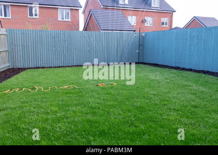 Sprinkler attached to a yellow hose being used to water a newly laid grass lawn on a new housing development Stock Photo