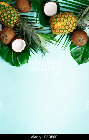 Exotic pineapples, ripe coconuts, tropical palm and green monstera leaves on blue background with copyspace for your text. Creative layout. Summer con Stock Photo