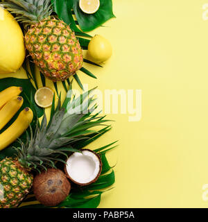 Exotic pineapples, coconuts, banana, melon, lemon, palm and monstera leaves on yellow, violet background with copyspace. Square crop. Creative layout. Stock Photo